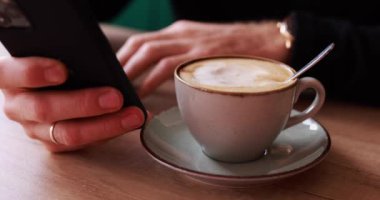 Bir kafede kahve içerken cep telefonu kullanan erkek eller.