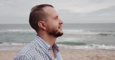 Deniz sahilinde güneş gözlüğü takan gülümseyen adam.