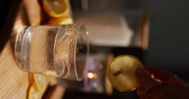 Kadın eli bir bardak suyu limonlu, dikey videolu, ağır çekimde alır.