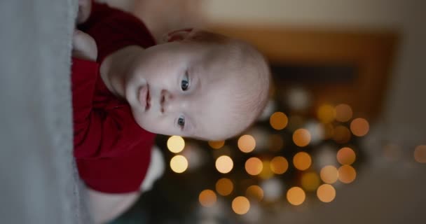 クリスマスツリーの背景 垂直ビデオで頭を保持しているベッドに横たわる新生児 — ストック動画