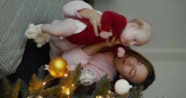 Noel ağacını süsleyen bir kadın yeni yıldan önce oğlunu kucağında tutuyor.