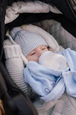 Küçük tatlı bir çocuk bebek arabasındaki bir şişeden süt içiyor.