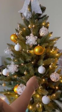Noel topunu ağaca asan tanınmamış bir kadın, yılbaşından önce dekore edilmiş bir oda, dikey video.