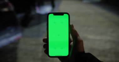 Gece park yerinde elinde yeşil ekranlı telefonu tutan adam.