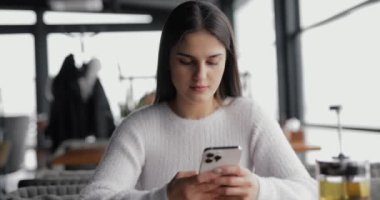 Kafedeki masada oturan beyaz elbiseli kadın akıllı telefon kullanıyor.