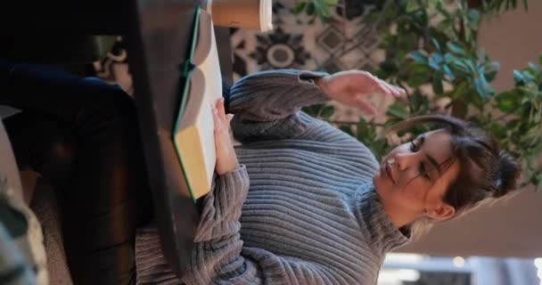 Молодая Женщина Читает Книгу Пьет Кофе Сидя Кафе Столом Вертикальное — стоковое видео