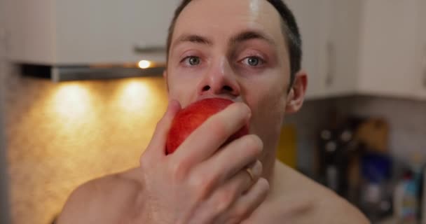 Ένας Άντρας Τρώει Ένα Κόκκινο Μήλο Στην Κουζίνα — Αρχείο Βίντεο