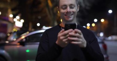 Gece şehir caddesinde akıllı telefon kullanan bir adam.