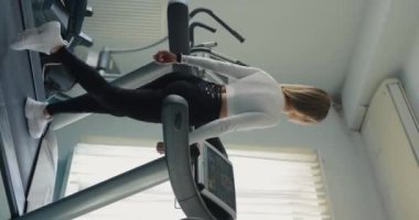 Spor salonunda koşu bandında egzersiz yapan bir kadın. Arka plan, dikey video.