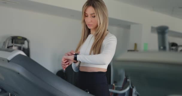 ジムでトレッドミルで運動しながら電子時計を使用する女性 — ストック動画