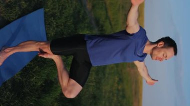 Yogacı adam doğada tek ayak üzerinde duruyor, dikey video.
