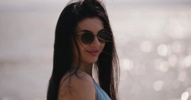 Güneş gözlüklü çekici kadın denize gülümsüyor, ağır çekimde.