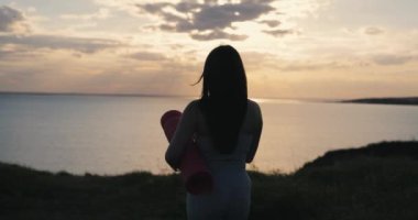 Spor elbiseli kadın silueti doğada yoga minderi taşıyor, ağır çekimde.