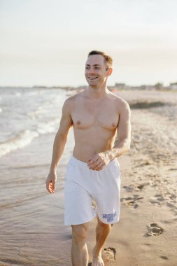 Beyaz şortlu, kumsala giden yakışıklı, beyaz bir adam.