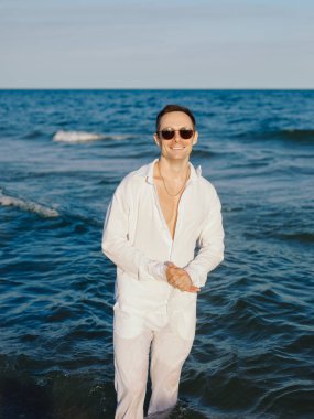 Denizde poz veren beyaz pantolonlu ve gömlekli zarif bir adam.