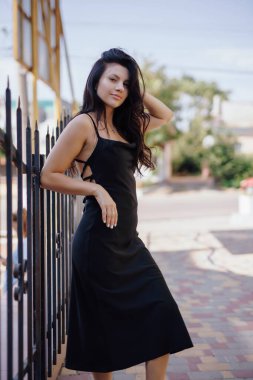 Şehirde siyah elbiseyle poz veren çekici bir kadın.