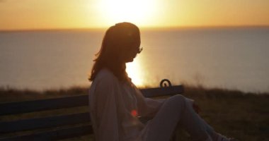 Oturup dinlenen, gün batımını seyreden kadın silueti, ağır çekim.