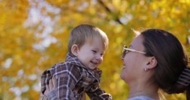 Yavaş çekim, bir anne güz parkında küçük mutlu bir çocuğu kucağına alıp fırlatıyor.