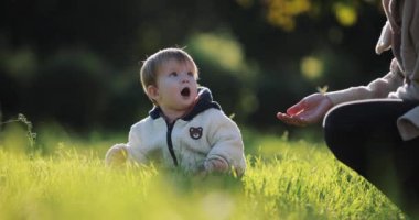 Yavaş çekim, tatlı çocuk sonbahar günü çimenlerde oturup oynuyor.