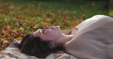 Düşen sonbahar yaprakları, yerde yatan bir kadının üzerine, ağır çekimde.