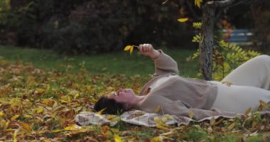 Düşen sonbahar yaprakları, yerde yatan bir kadının üzerine, ağır çekimde.