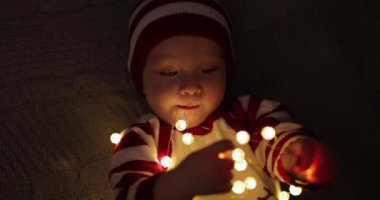 Noel Baba kostümlü küçük çocuk Noel 'den önce evde çelenkle oynuyor.