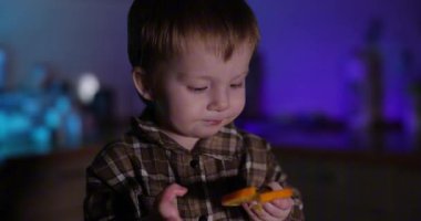 Mutfakta portakal yiyen bir çocuk, mavi ışık arka planda.