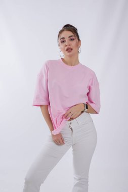 Beyaz arka planda poz veren pembe tişörtlü bir kadın.