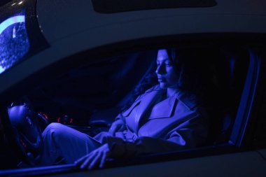 Geceleri mavi ışıkta arabada poz veren seksi kadın.