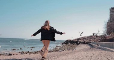 Yavaş çekim yapan kadın martıları deniz kıyısına dağıtıyor.