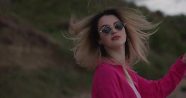 Büyüleyici, şık bir kadın yüzünü doğaya doğru çeviriyor, saçlarını savuruyor, ağır çekimde.