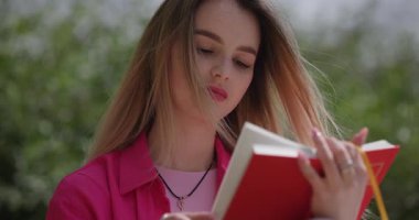Pembe elbiseli kadın dışarıda kırmızı kitap okuyor.