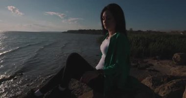 Deniz kenarındaki kayalarda oturan akıllı bir kız.