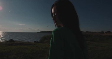 Denizin kenarında durup saçlarına dokunan bir kadın silueti.