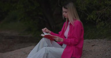 Pembe elbiseli kadın dışarıda kırmızı kitap okuyor.