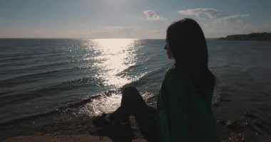 Deniz kenarındaki bir kayada oturan kız manzaranın tadını çıkarıyor.