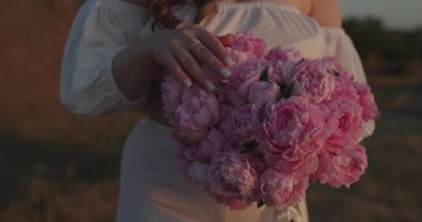 Gün batımında denizin üstünde elinde bir buket çiçek tutan tanınmamış bir kadın.