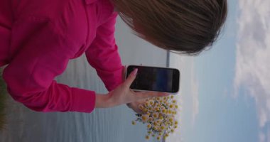 Kız telefonunda toplanmış bir buket papatyanın fotoğrafını çekiyor, dikey video.