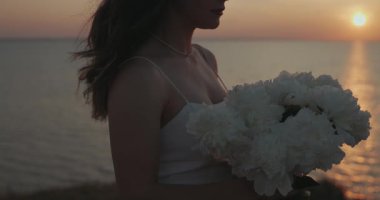 Mutlu kadın, gün batımında denizin üstünde bir buket çiçeği koklar.