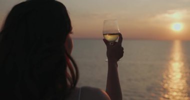 Gün batımında denizin üstündeki tepede şarap içen bir kadın.