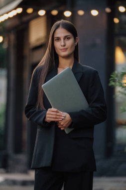 Klasik takım elbiseli bir kadın şehirde dizüstü bilgisayar tutuyor.