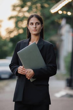 Klasik takım elbiseli bir kadın şehirde dizüstü bilgisayar tutuyor.