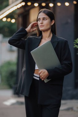 Klasik takım elbiseli bir kadın şehirde dizüstü bilgisayar tutuyor.