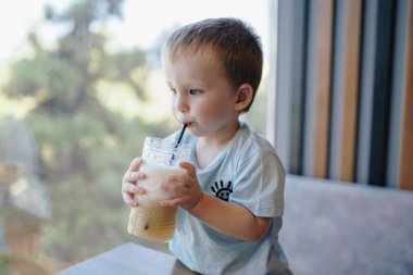 Küçük bir çocuk kafede samanla limonata içiyor.