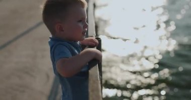 Küçük çocuk bir iskelede çitlere yaslanmış denize bakıyor.