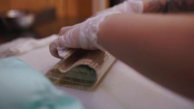 Şefin elleri bambu hasırında suşi rulosu hazırlıyor.