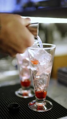 Barmen elleri barda pembe kokteyller hazırlıyor, likör dökülüyor, dikey video.