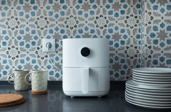 Modern ev mutfağında beyaz hava kızartma makinesi, kupalar ve bulaşıklar. Teknoloji ev yapımı akıllı aygıt
