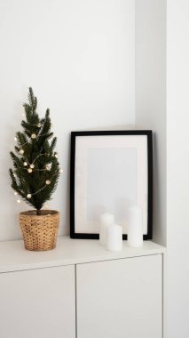 Model poster çerçevesi, ışıklandırmalı Noel ağacı ve modern minimalist oturma odasındaki mumlar, dikey