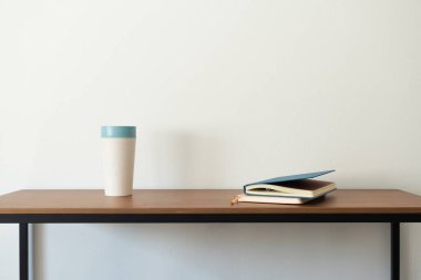 Defterler ve kahve fincanı ahşap masanın üstünde, minimalist iç mekan. Ya çalış ya da okula geri dön.